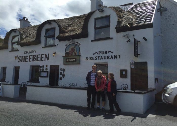 Three people standing in front of cronin's sheebeen pub & restaurant with a thatched roof.