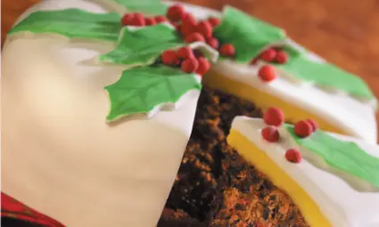 A close-up of a traditional fruitcake with white icing and holly berry decoration.