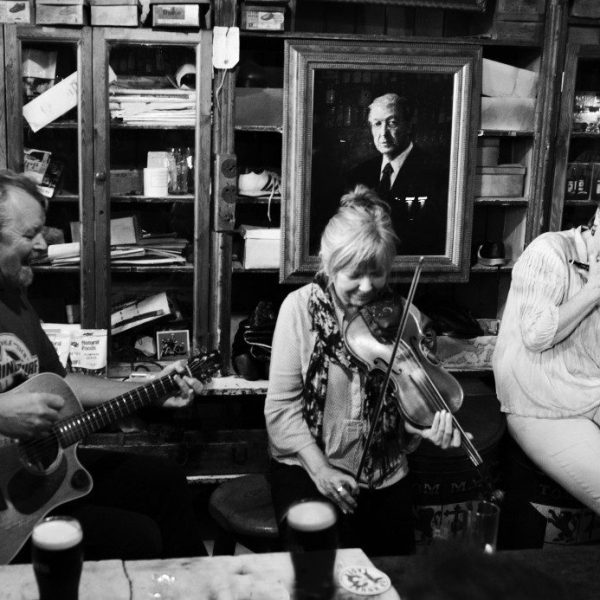 Musicians performing informally in a cozy bar setting, surrounded by wooden decor and a portrait on the wall.