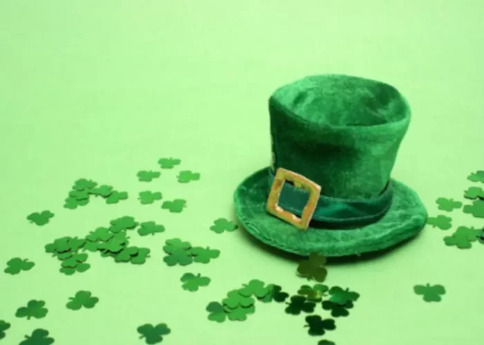 A green leprechaun hat surrounded by shamrock confetti on a green background.