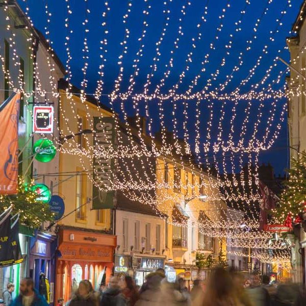 A bustling street adorned with festive lights and a christmas tree, evoking a holiday atmosphere in an urban setting.