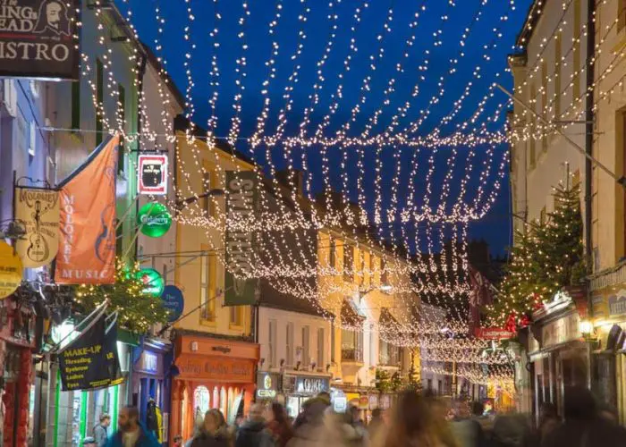 A bustling street adorned with festive lights and a christmas tree, evoking a holiday atmosphere in an urban setting.