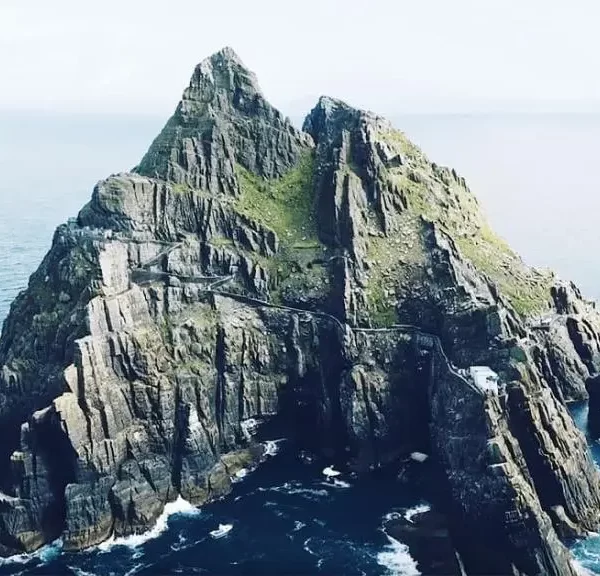 Aerial view of a steep, rocky island with a staircase along its cliff, set against a calm ocean.