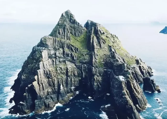Aerial view of a steep, rocky island with a staircase along its cliff, set against a calm ocean.