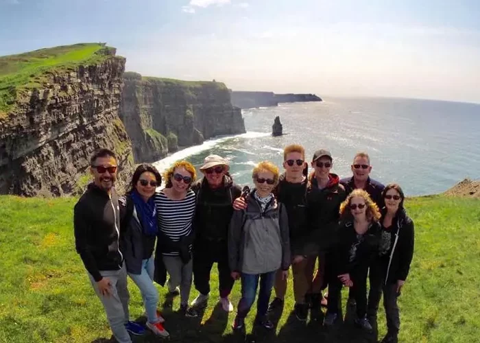 A group of guests on an Overland small-group Ireland tour pose for a photo on a sunny day with the famous Cliffs of Moher in County Clare, Ireland, behind them. The green grass covering the clifftops, the rugged cliff faces, and the roaring Atlantic Ocean in the background are quintessential images of Ireland’s Wild Atlantic Way.
