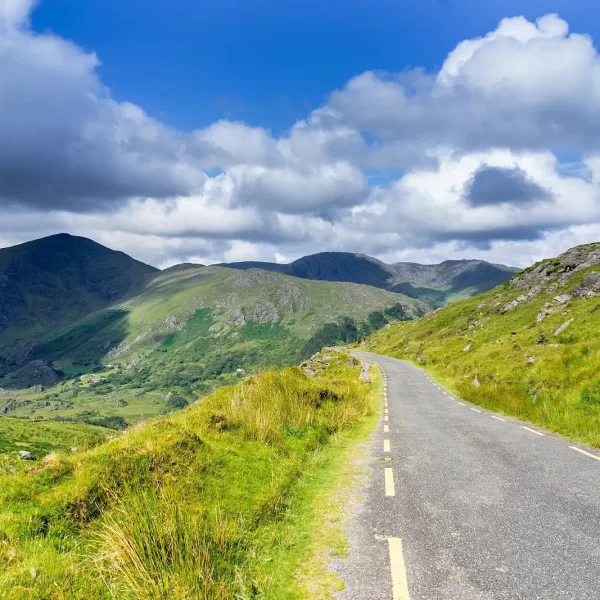 A scenic, winding road through a hilly landscape under a partly cloudy sky.