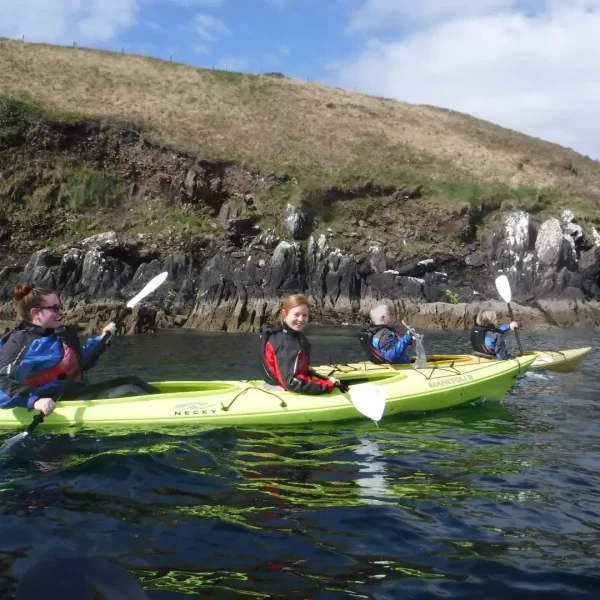 Three people kayaking near a rocky shore.