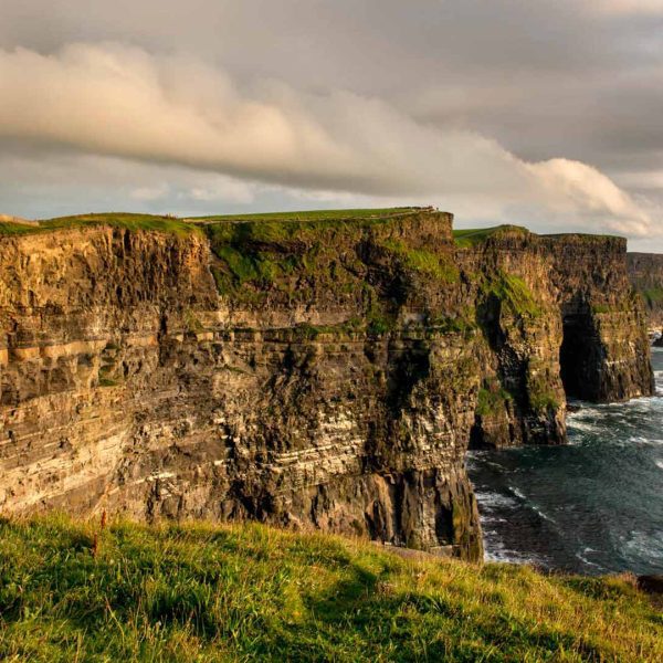 Sweeping view of the cliffs of moher under a cloudy sky at sunset.