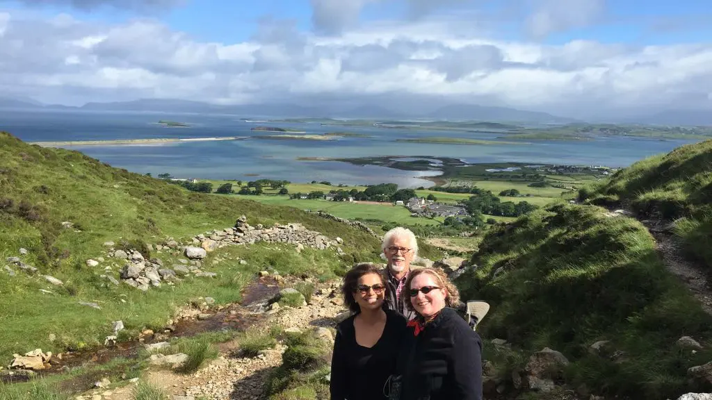 Four individuals posing for a photo on a hillside with a panoramic view of a coastal landscape and overcast skies in the background.