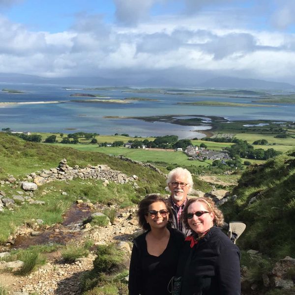 Four individuals posing for a photo on a hillside with a panoramic view of a coastal landscape and overcast skies in the background.