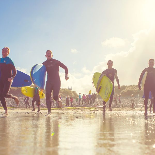 Group of surfers carrying boards on a sunny beach.