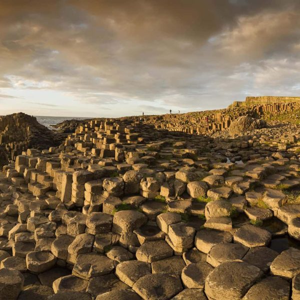 Sunset over the giant's causeway with hexagonal basalt columns near the coast and a person standing in the distance.