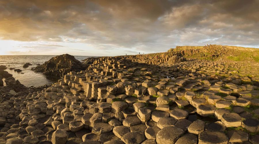 Sunset over the giant's causeway with hexagonal basalt columns near the coast and a person standing in the distance.