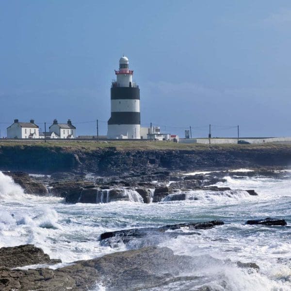 Hook Head Lighthouse in County Wexford, Ireland, stands on a rocky coastline with rough sea waves crashing onto the shore.
