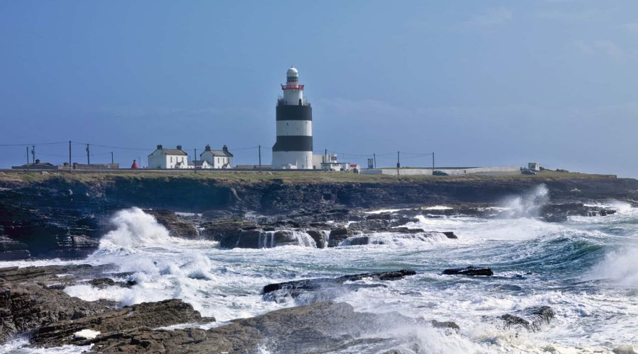 Lighthouse on a rocky coastline with rough sea waves crashing onto the shore.