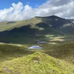 Rolling hills with a serene lake nestled in a valley, under a partly cloudy sky.
