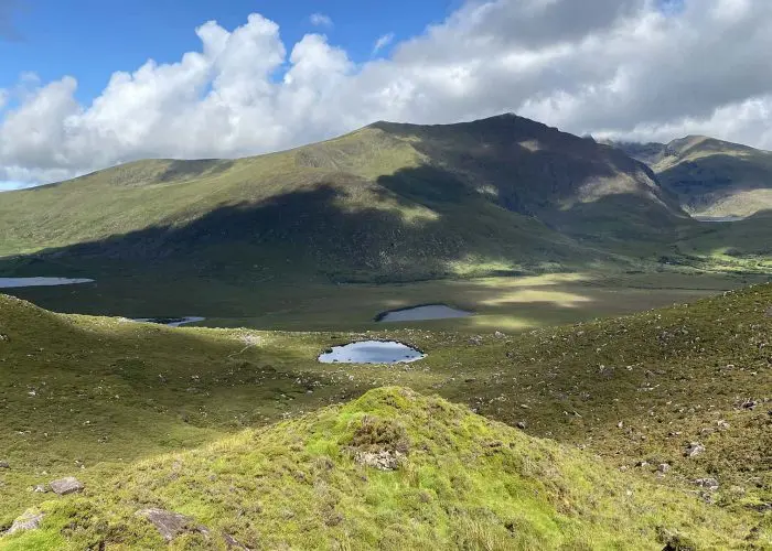 Rolling hills with a serene lake nestled in a valley, under a partly cloudy sky.