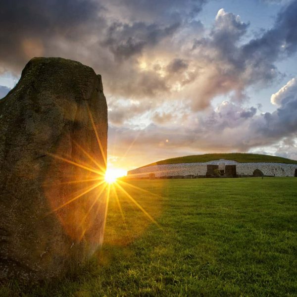 Ancient stone structure at sunset with sunbeams peering around the monolith.