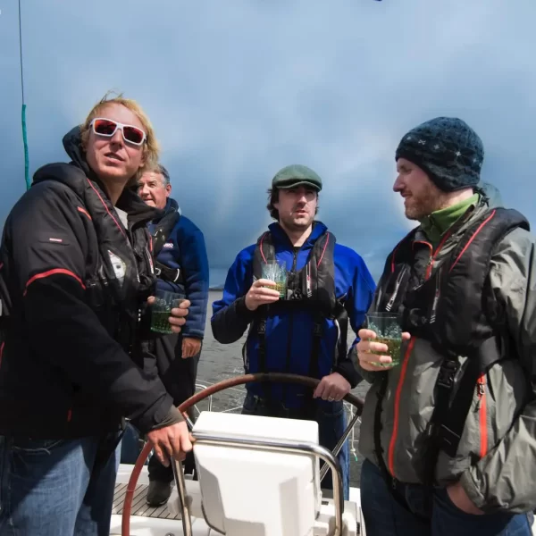 Group of people enjoying drinks on a boat with overcast skies in the background.