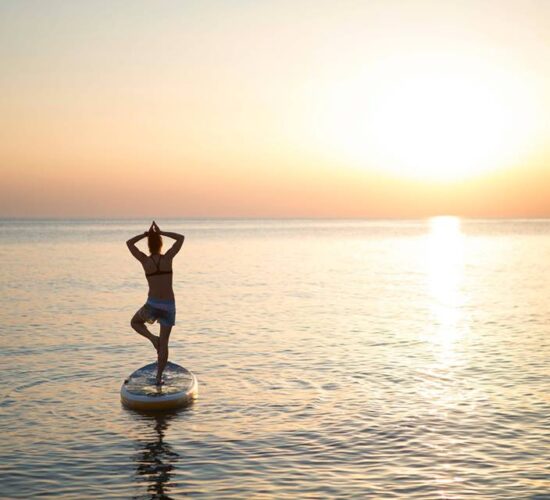 Person practicing yoga on a paddleboard at sea during sunset on an Ireland tour.