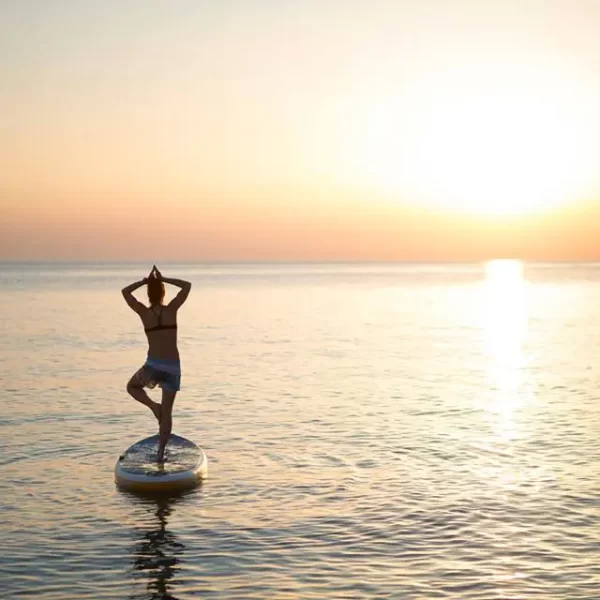 A person practicing yoga on a paddleboard at sunset.