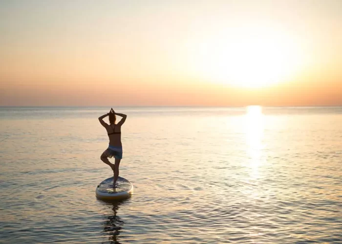 A person practicing yoga on a paddleboard at sunset.