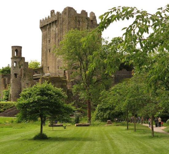 Medieval castle in Ireland, surrounded by greenery with visitors strolling along a path.