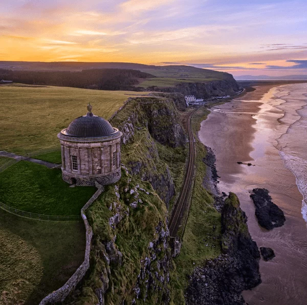 Aerial view of a historic building on a cliff overlooking a beach at sunset.