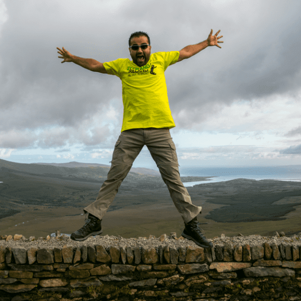 Man jumping above a stone wall with a scenic landscape in the background.