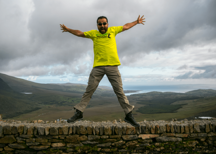 Man jumping above a stone wall with a scenic landscape in the background.