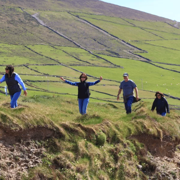 Tourists hiking along a grassy hillside with a view of farmlands in the background.