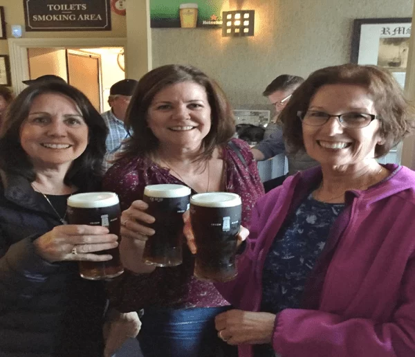 Three women smiling and holding pints in a pub.