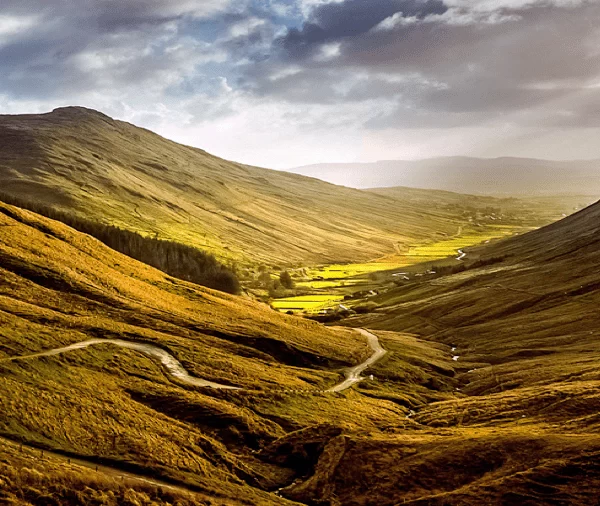 Golden sunlight illuminating a winding valley road between rolling hills.