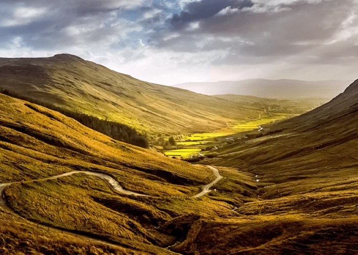 Golden sunlight illuminating a winding valley road between rolling hills.