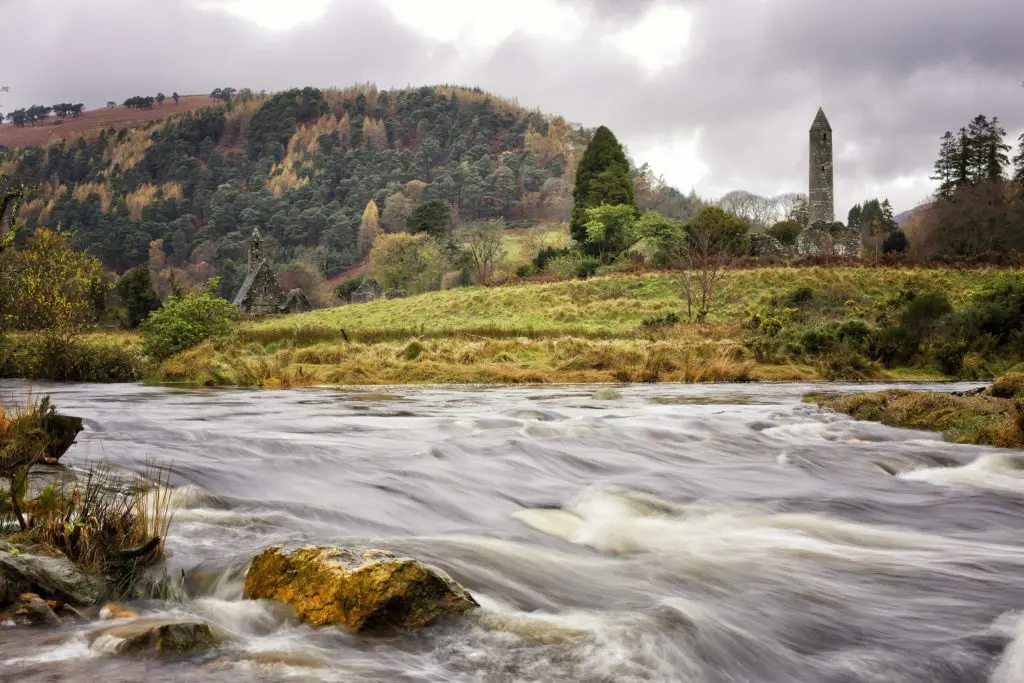 A flowing river with a historical tower amidst autumn-colored trees on a cloudy day.