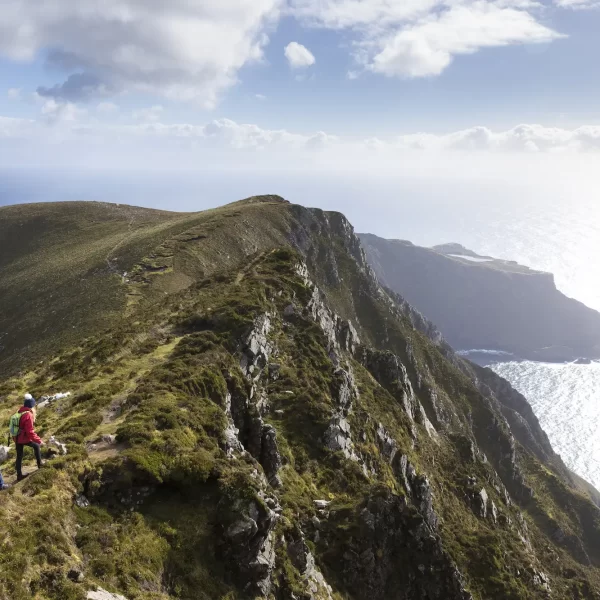 Two hikers walking on a mountain ridge overlooking the sea.