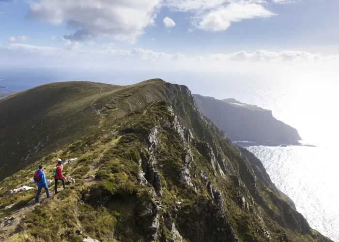 Two hikers walking on a mountain ridge overlooking the sea.