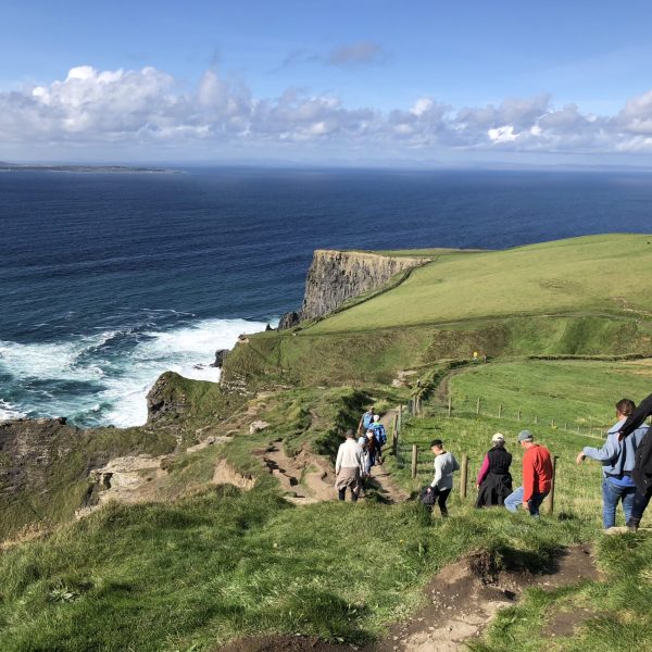 Tourists walking down a coastal path near steep cliffs overlooking the ocean.