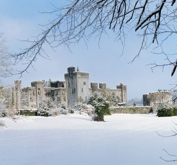 A snow-covered castle on a clear day with bare branches in the foreground.