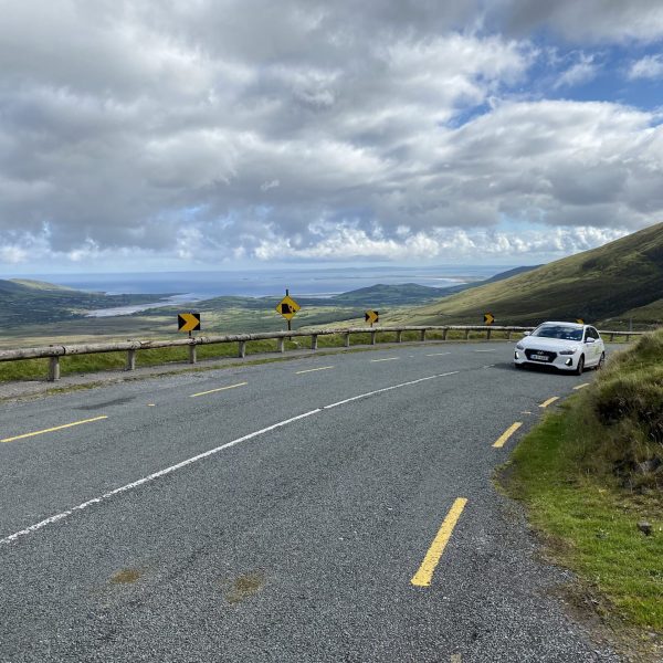 A white car parked on a curving mountain road with scenic views and warning road signs.