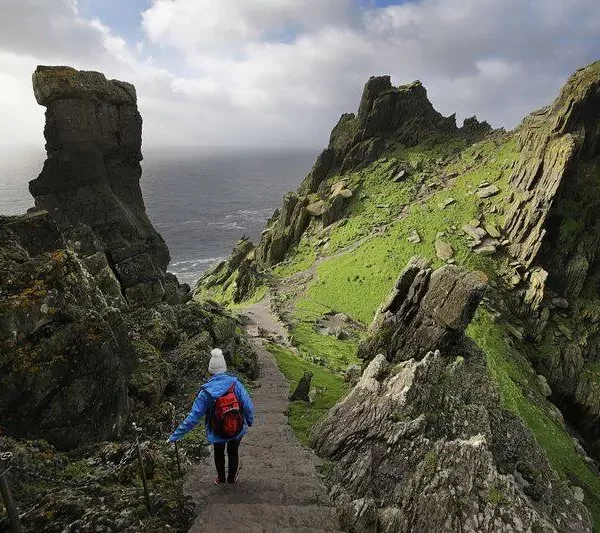 A person hiking on a rocky path between steep cliffs by the sea.