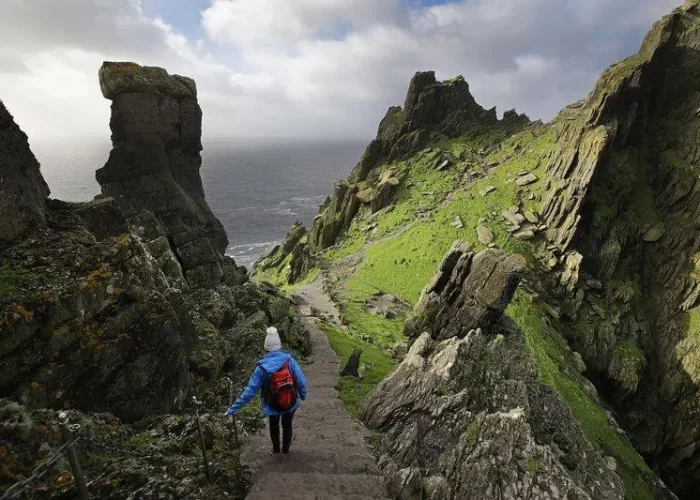 A person hiking on a rocky path between steep cliffs by the sea.