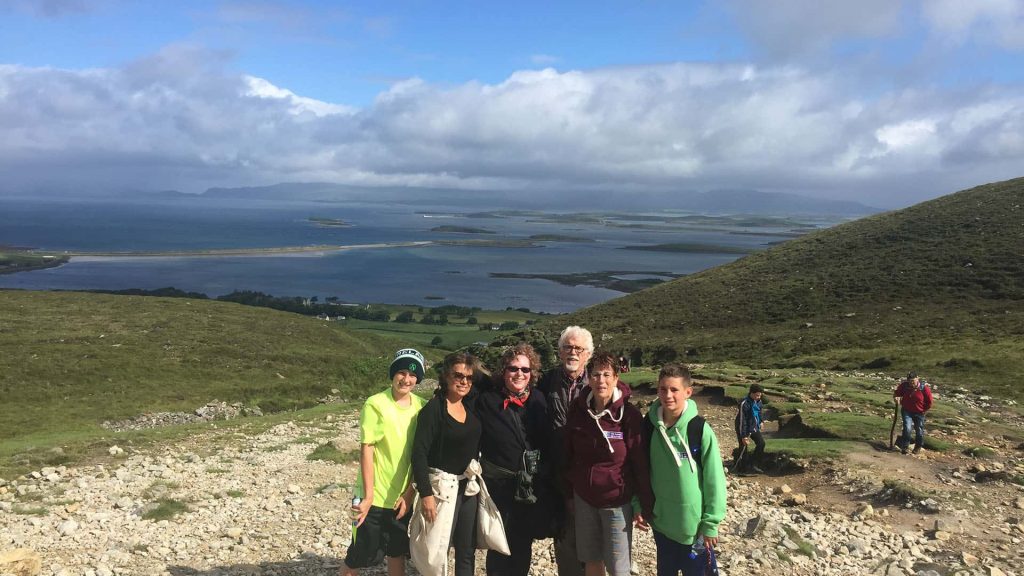 Group of hikers posing for a photo with scenic hills and a water body in the background.