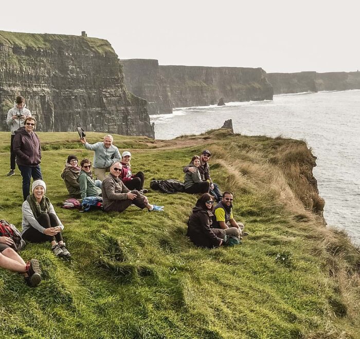 Group of people sitting on grass overlooking the cliffs of Moher, enjoying a private tour in Ireland.