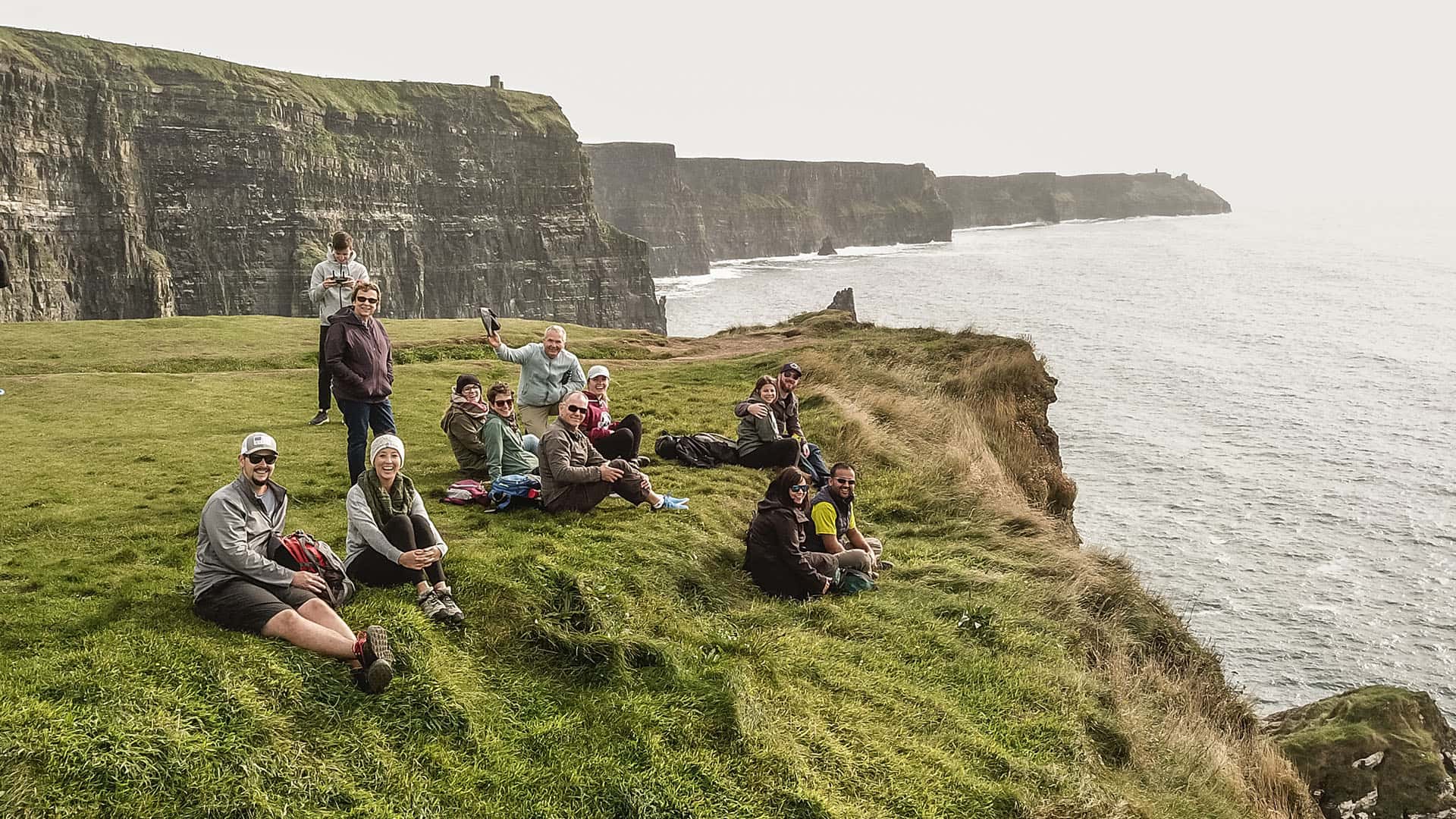 Group of people sitting on grass overlooking the cliffs of Moher, enjoying a private tour in Ireland.