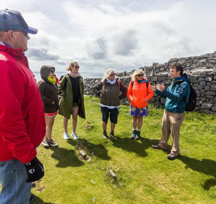 Group of tourists on a self-drive tour in Ireland, listening to a guide at an outdoor historical site.