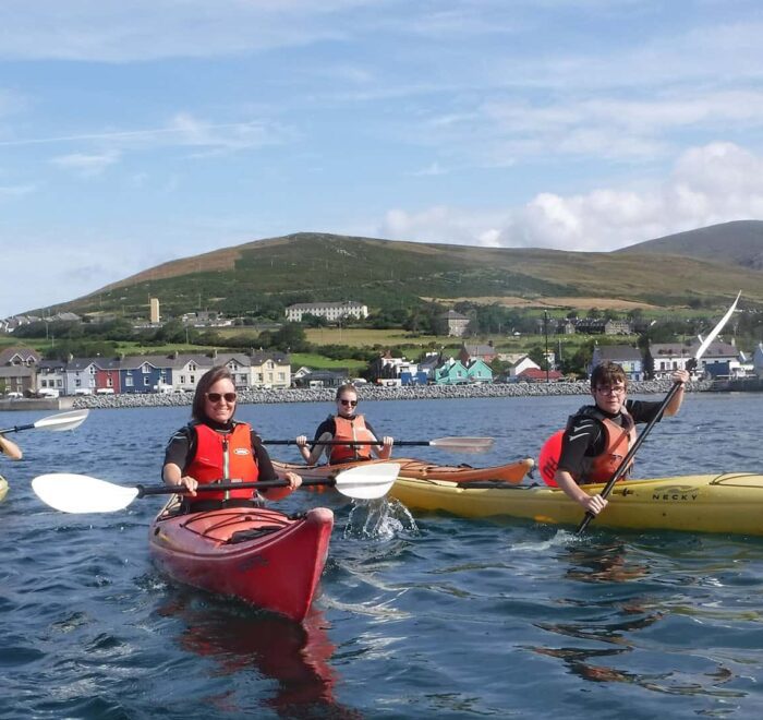Group of kayakers on a sunny day with a coastal town in Ireland Tours in the background.