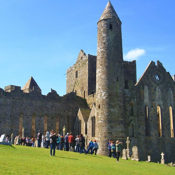 Tourists visiting the ruins of a medieval cathedral with a round tower on a sunny day.