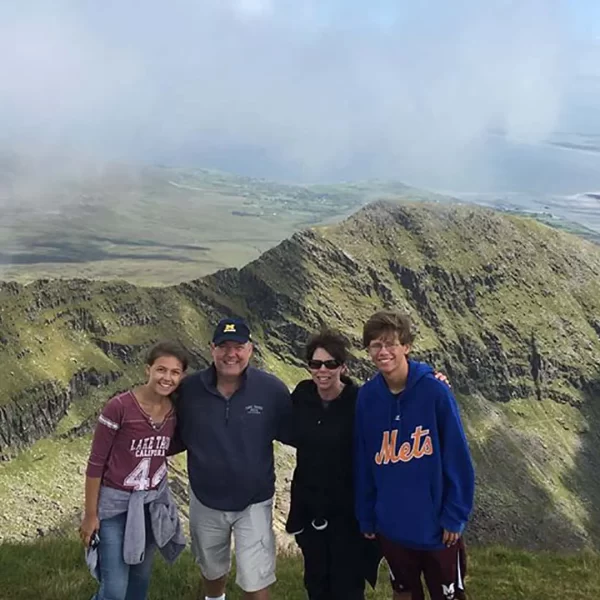 Group of four people posing for a photo on a mountain with a scenic river and valley in the background.