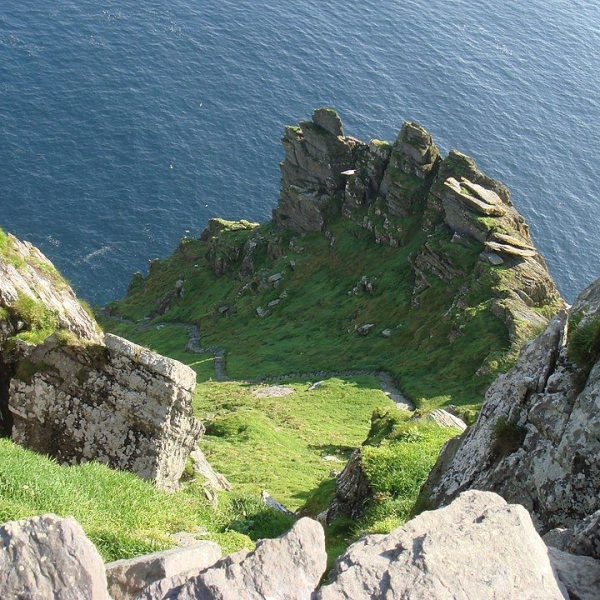 A rugged cliffside with green grass overlooking a deep blue sea.